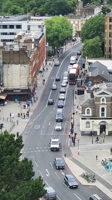 An aerial view of a busy residential street in Hornsey, featuring a row of parked cars along the curb and moving vehicles including a red double-decker bus, with pedestrians walking on the sidewalks a