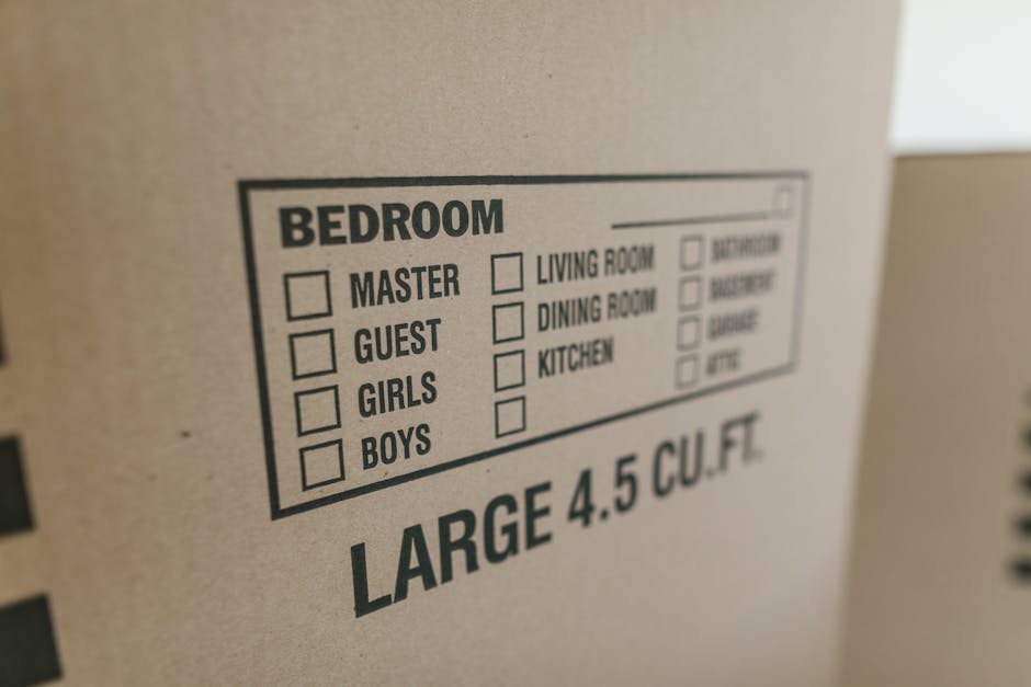 A close-up photograph of a cardboard box featuring a printed checklist for room packing categories, including options for bedroom, with checkboxes next to labels such as 'Master,' 'Guest,' 'Girls,' and 'Boys,' and additional categories for other rooms like living room, dining room, and kitchen, all within a label box. The box is situated on a flat surface, likely part of a home relocation or packing process managed by Man with Van Hornsey, with visible text indicating it contains large items of 4.5 cubic feet. The background shows a plain, indoor environment with soft lighting, emphasizing the label's details as part of the packing and moving logistics involved in house removals and furniture transport.